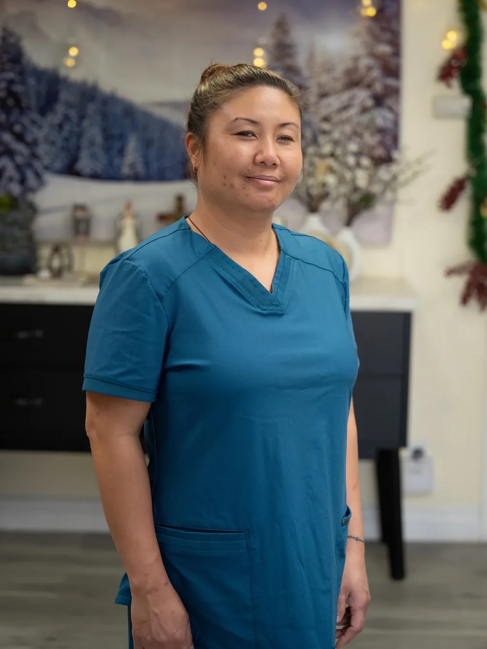 Caregiver in teal medical scrubs smiling in residential care facility living room